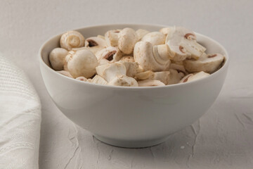 Sliced fresh champignons in a white porcelain bowl, next to a white towel