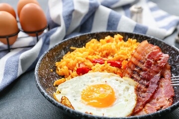 Plate with tasty egg, bacon and rice on dark background