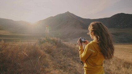 Back view of a female photographer holding a camera in her hands and photographing a model against a background of mountains
