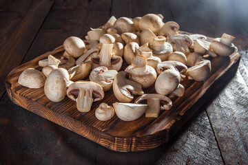 Fresh sliced mushrooms lie on a dark cutting board on a dark wooden background