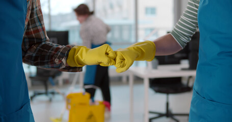 Cropped shot of janitors bumping fists in rubber gloves cleaning office