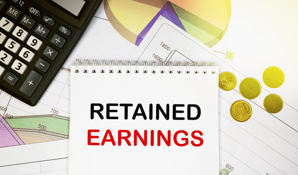 Retained earnings on notepad with calculator, coins, graphics on financial report. Business and financial concept