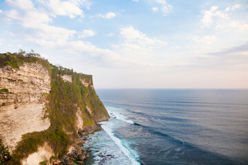 View of Uluwatu cliff with pavilion and blue sea in Bali, Indonesia. Rocky cliff and sea waves.
