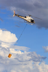 A firefighting helicopter high in the sky, towing a water bucket