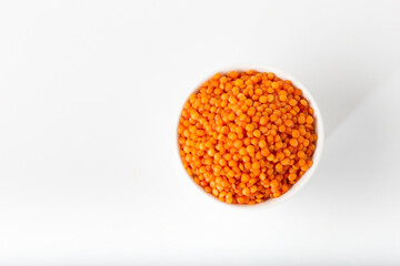 Red lentils in white bowl on white background.