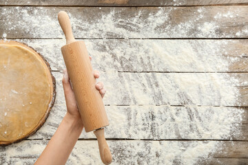 Female hand with rolling pin on wooden background