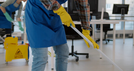 Close up of asian janitor in apron and rubber gloves wiping floor in office with mop