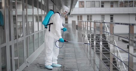 Worker in virus protective suit and mask disinfecting building of coronavirus with sprayer