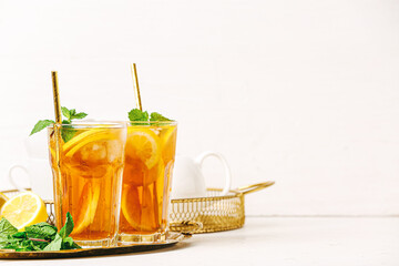 Glasses of cold black tea with lemon on light background