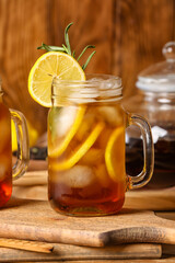 Mason jar of cold black tea with lemon on wooden background