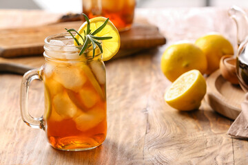 Mason jar of cold black tea with lemon on wooden background