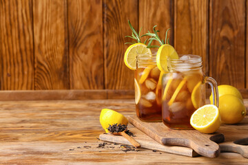 Mason jars of cold black tea with lemon on wooden background