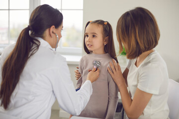 Family doctor listens with a stethoscope to a little girl who came for a medical examination with her mother. Female therapist diagnoses the symptoms of the disease in a child in the hospital.
