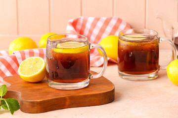 Cups of cold black tea with lemon on color background