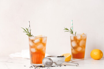 Glasses of cold black tea with lemon on light background