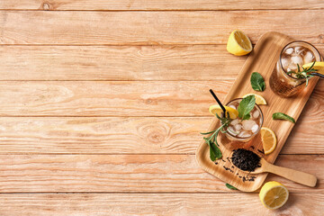 Glasses of cold black tea with lemon on wooden background
