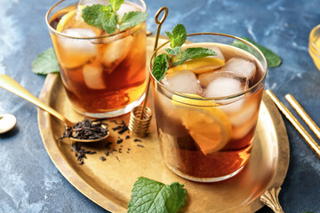 Glasses of cold black tea with lemon on color background