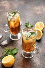 Cups of cold black tea with lemon on grunge background