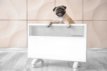 Cute pug dog with electric convector heater at home. Concept of heating season