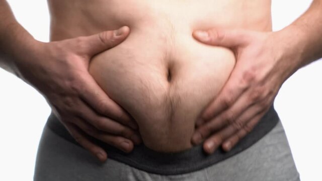 Fat man with a big belly shows his fat on a white screen. Male stomach, overweight.