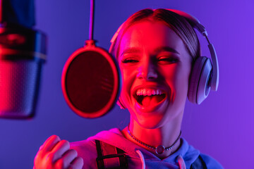 young singer in wireless headphones recording song while singing in microphone on blurred foreground