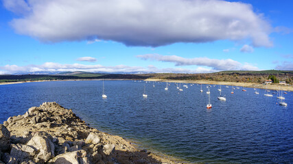 Atazar Reservoir with pleasure boats to navigate. Panoramic with blue sky and white clouds. Madrid.
