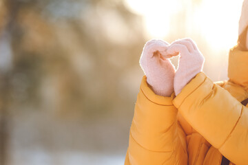 Young woman in warm clothes making heart shape with her hands on winter day