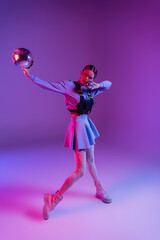full length of woman in skirt holding disco balls on purple