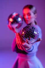 shiny disco ball in hand of trendy woman on purple and blurred background