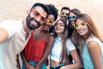 Group of teenagers taking a funny selfie wearing weird colorful sunglasses. Young people having fun...