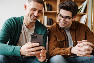 Happy young gay couple using mobile phone