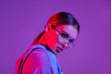young stylish woman in sunglasses looking at camera isolated on purple