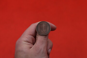 Old copper coin of colonial India half anna in hand on red background