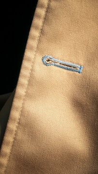 Ojal de bot&oacute;n con pespunte de hilo azul en gabardina beige