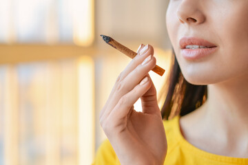 Young woman smoking cigarette at home, closeup