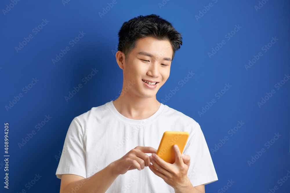 Poster casually dressed student standing isolated on blue background looking at screen of smart phone, brow
