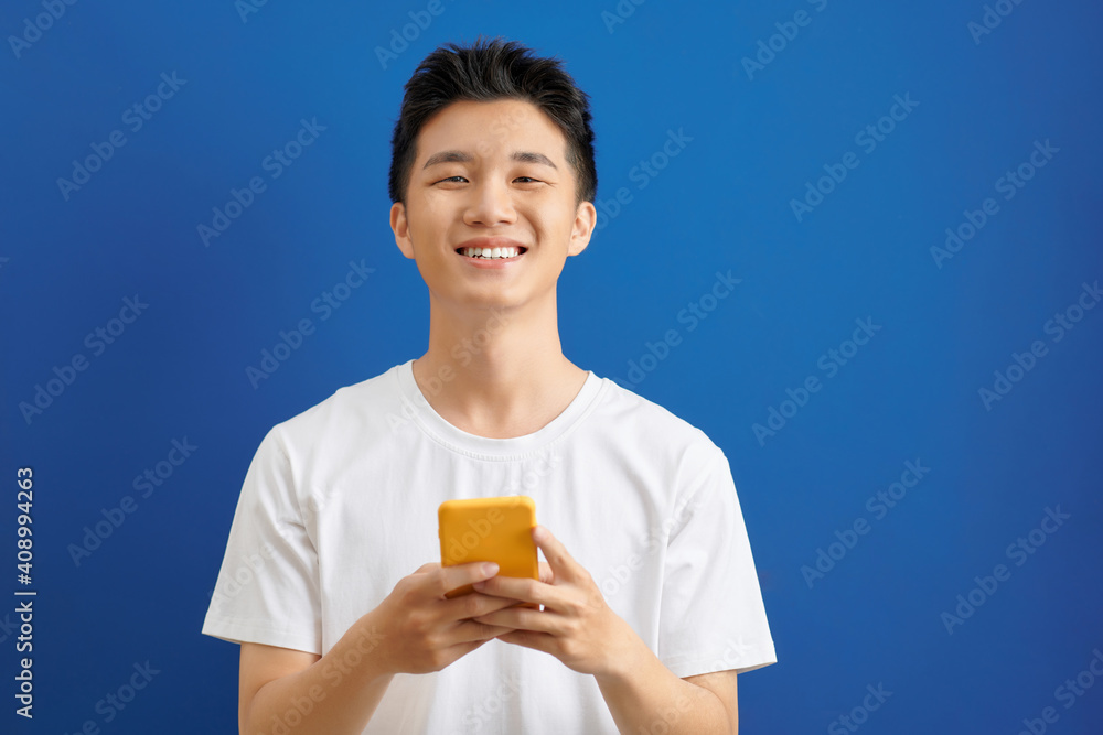 Poster casually dressed student standing isolated on blue background looking at screen of smart phone, brow