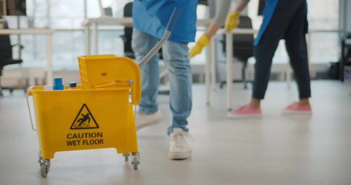 Janitor taking detergent spray from yellow cart to clean office windows