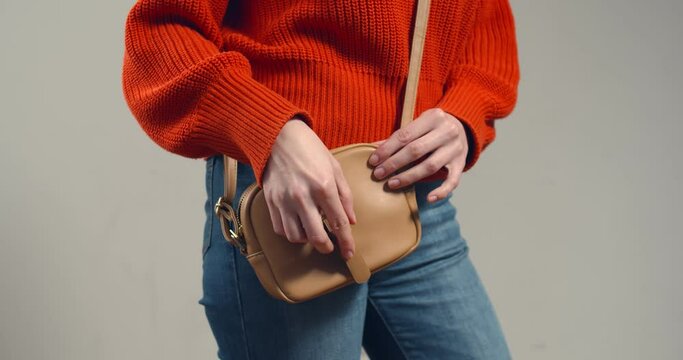 Close-up of young woman putting condom in handbag isolated on grey background