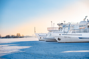 Fototapeta na wymiar Passenger ships in dock on frozen river. Boats on ice