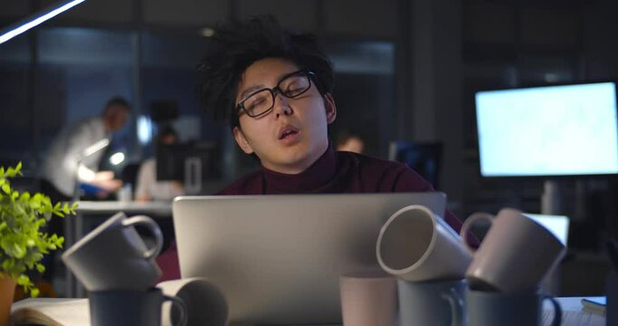 Tired businessman falling asleep at table with computer and coffee cup during night time in office