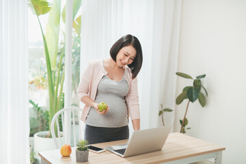 Beautiful pregnant woman with laptop and apple at home