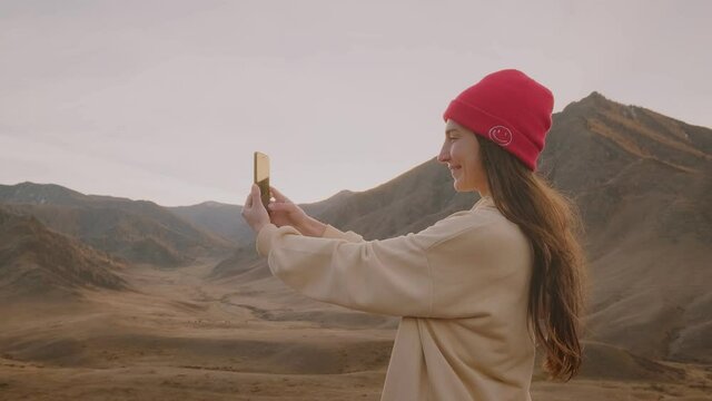 Young woman traveler makes a selfie against the backdrop of a mountain valley and wildlife