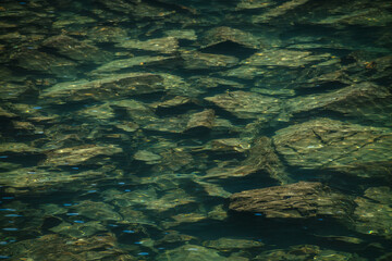 Meditative ripple of mountain lake. Beautiful relaxing background of stony bottom in turquoise transparent water of glacial lake in sunlight. Sunny backdrop with many stones in green clear water.