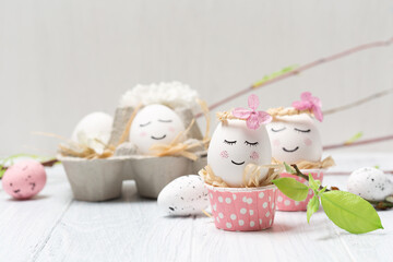Easter holiday concept with cute handmade white eggs, tree branches, quail feathers and spring flowers on white wooden background.