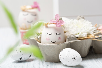 Easter holiday concept with cute handmade white eggs, tree branches, quail feathers and spring flowers on white wooden background.