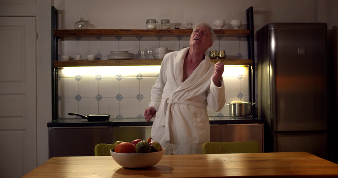 Funny Senior Man Wearing Bathrobe Dancing In Modern Kitchen Alone