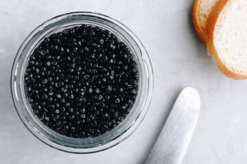 Black caviar in glass jar on white stone background. Top view, copy space