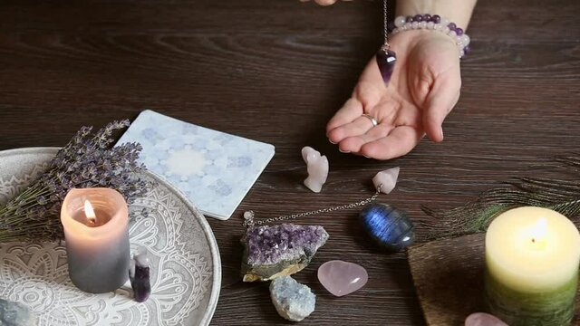 Close up of  hand holding and using amethyst crystal pendulum on silver chain. Fortune telling concept.