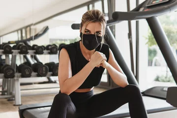 Gordijnen Young athletic woman wearing a prevention face mask during her fitness workout. © blackday